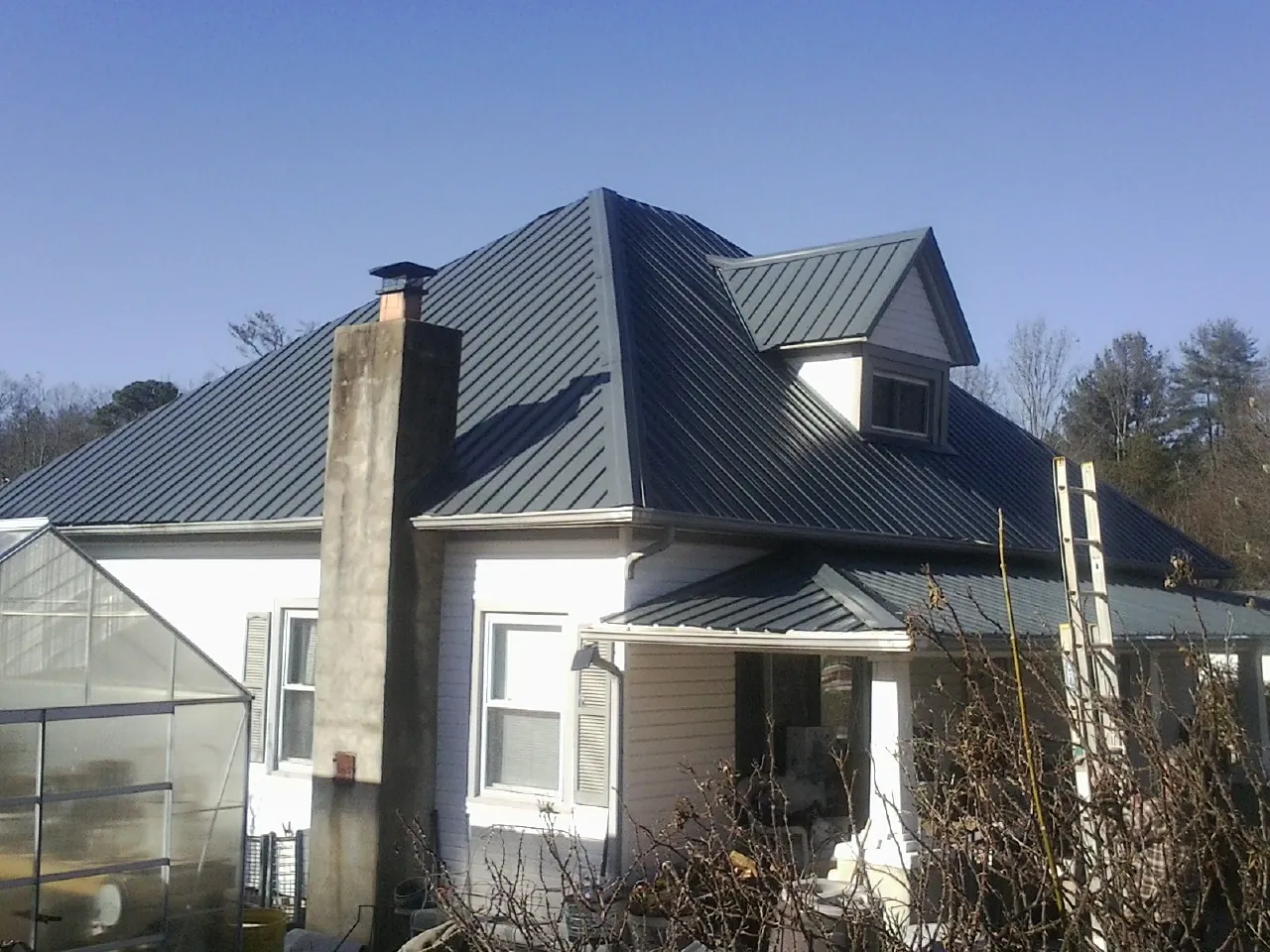 Dark blue standing seam metal roof on a white farmhouse with dormer — Slate & Tile Roof Repair by Roofing Brothers in Williams Bay