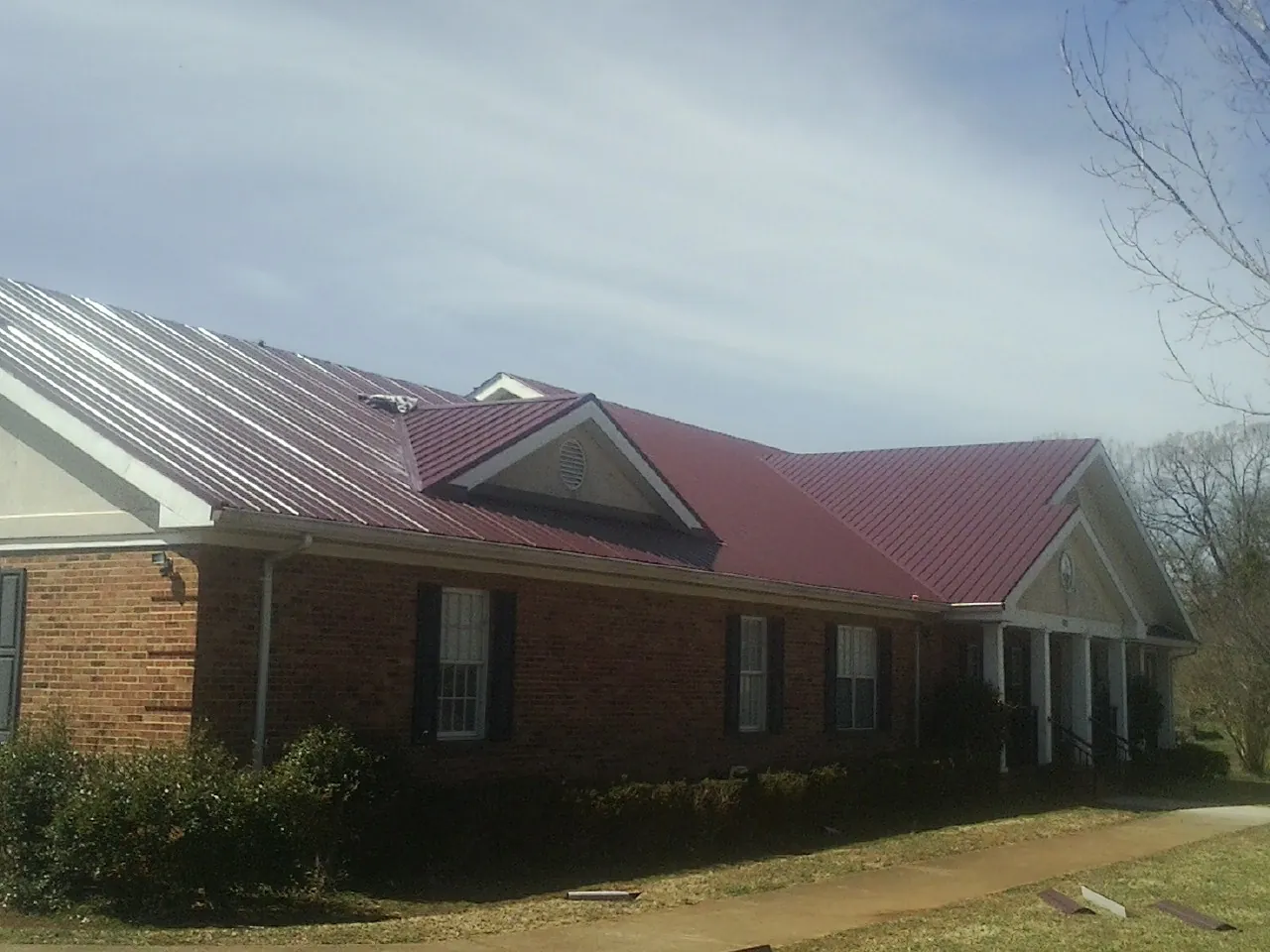 Red metal roof with gabled entries on a long brick building, from a Hail Damage Roof Repair job in Williams Bay