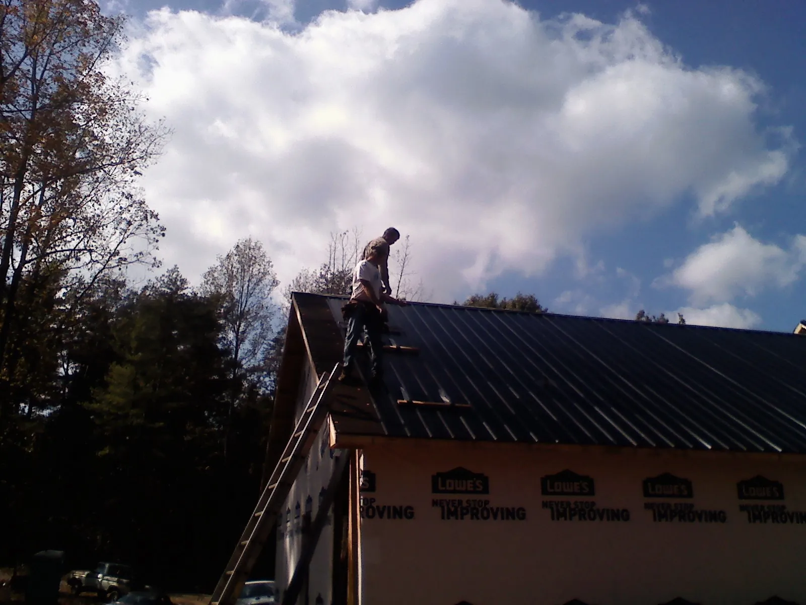 Roofer fastening dark metal panels high against a cloudy sky, from a Roof Inspection job in Williams Bay