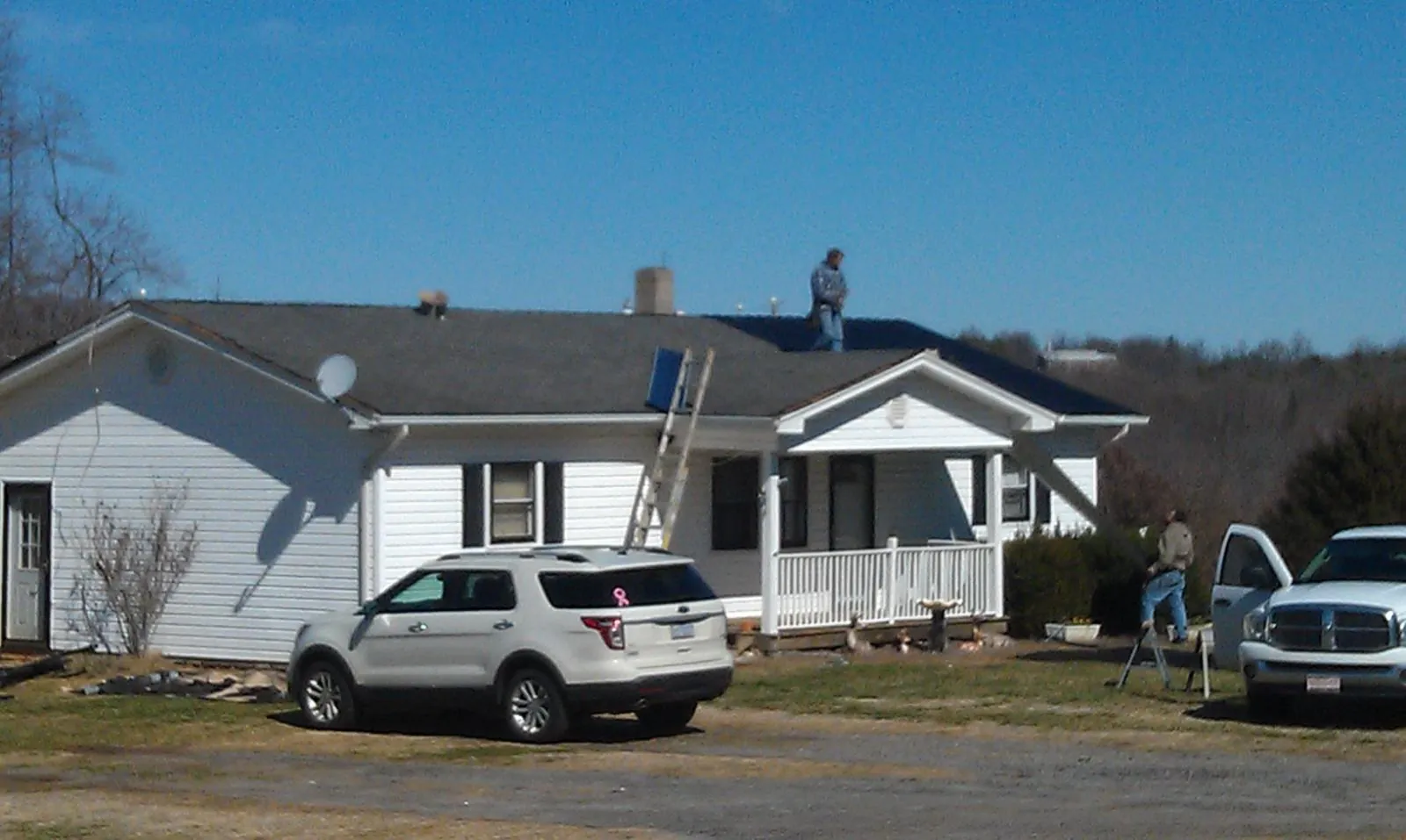 Roofers stripping shingles from a white ranch house roof in Williams Bay