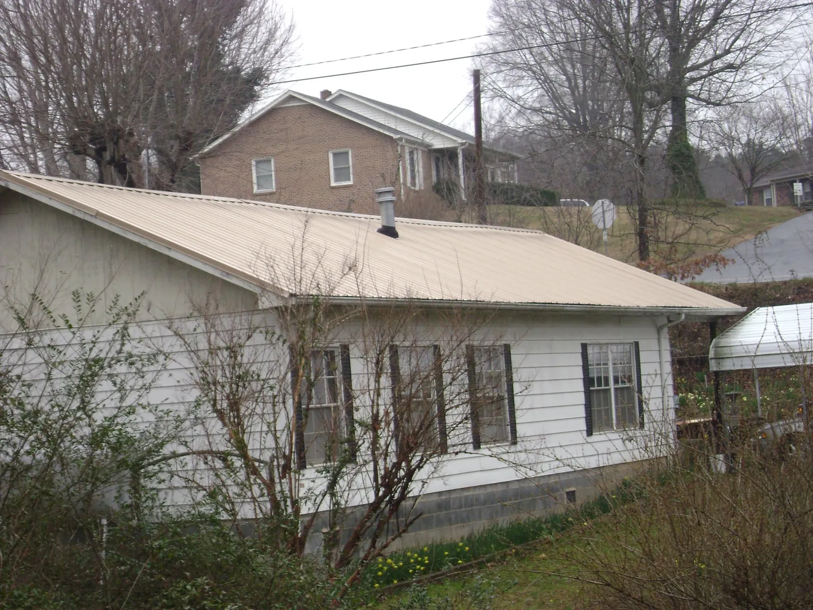 Tan metal roof on a white sided house set into a hillside — Commercial Roofing by Roofing Brothers in Williams Bay