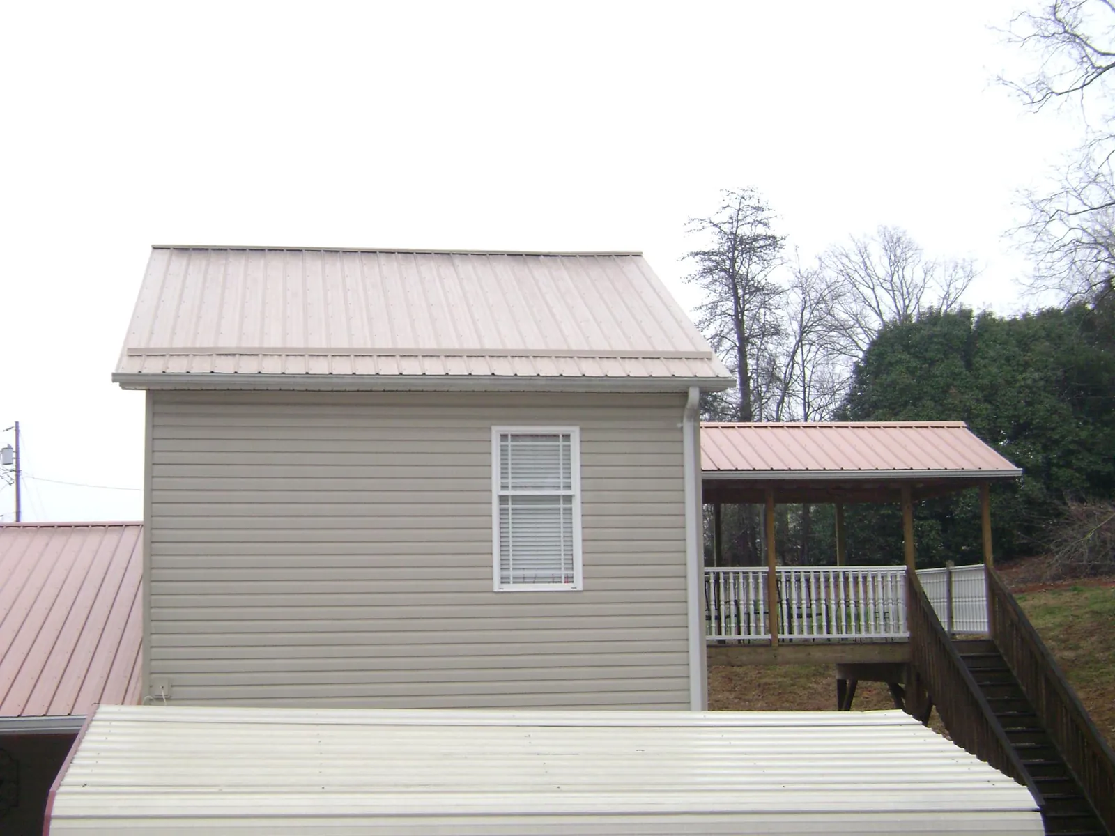 Tan metal roofs on a two story addition and attached porch, from a Roof Replacement job in Williams Bay